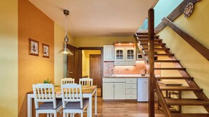 A kitchen with wooden cabinets, a dining area with white chairs, and a wooden staircase. - Vysoké nad Jizerou by Interhome (Vysoké nad Jizerou)