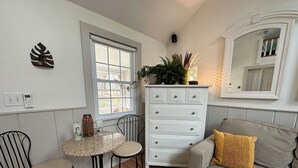 Un salon avec un canapé blanc, une table ronde accompagnée de deux chaises, une commode blanche et un miroir placé au-dessus du canapé.