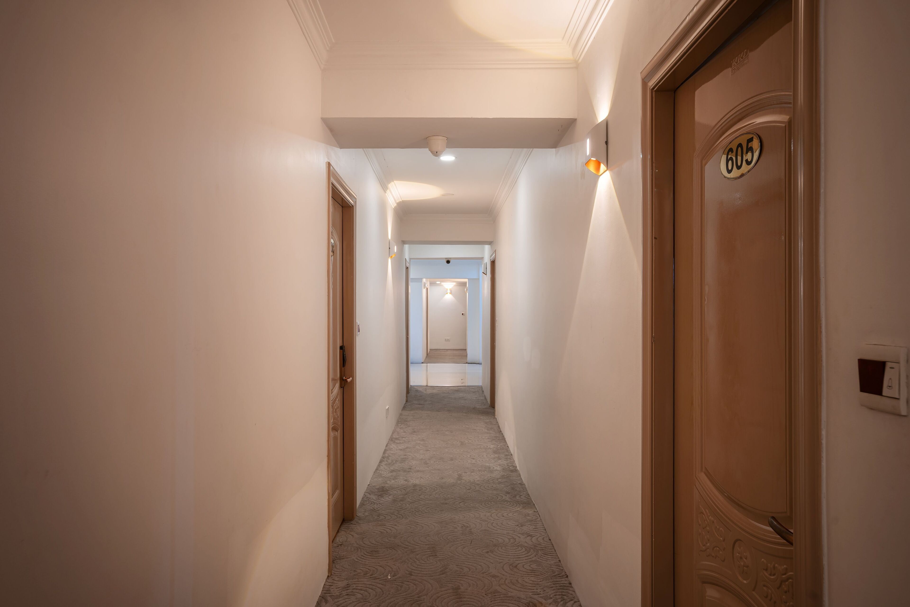 A hallway with a carpeted floor, a door with the number 605, and a light fixture on the wall.