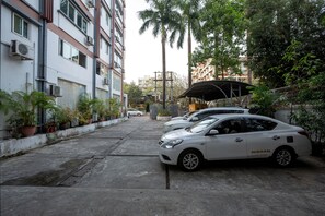 A parking area with two white cars, a covered structure, and potted plants along the building's facade. - Green Star Hotel Yangon (Yangon)