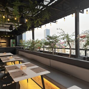 An outdoor seating area with tables, benches, and hanging plants. - Green Star Hotel Yangon (Yangon)