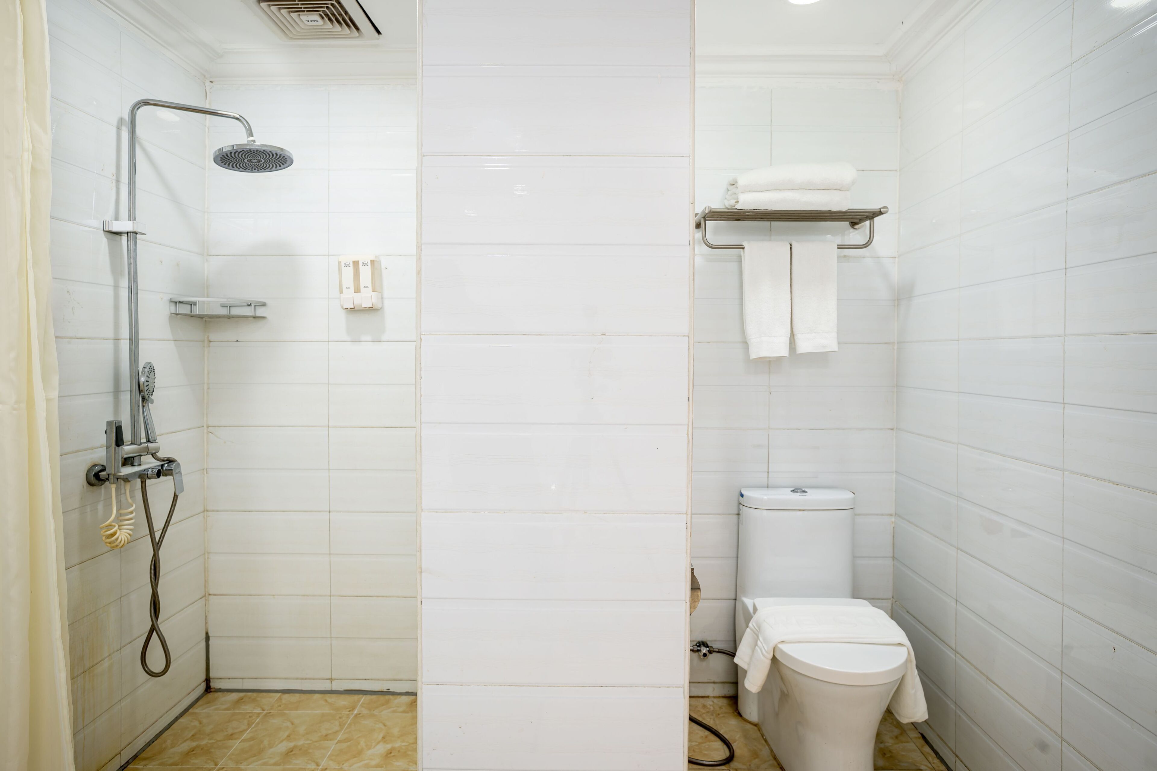 Une petite salle de bain propre, avec des carreaux blancs, une douche, des toilettes et un porte-serviettes.