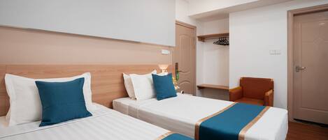 A hotel room with two beds, a chair, a wardrobe, and a door.