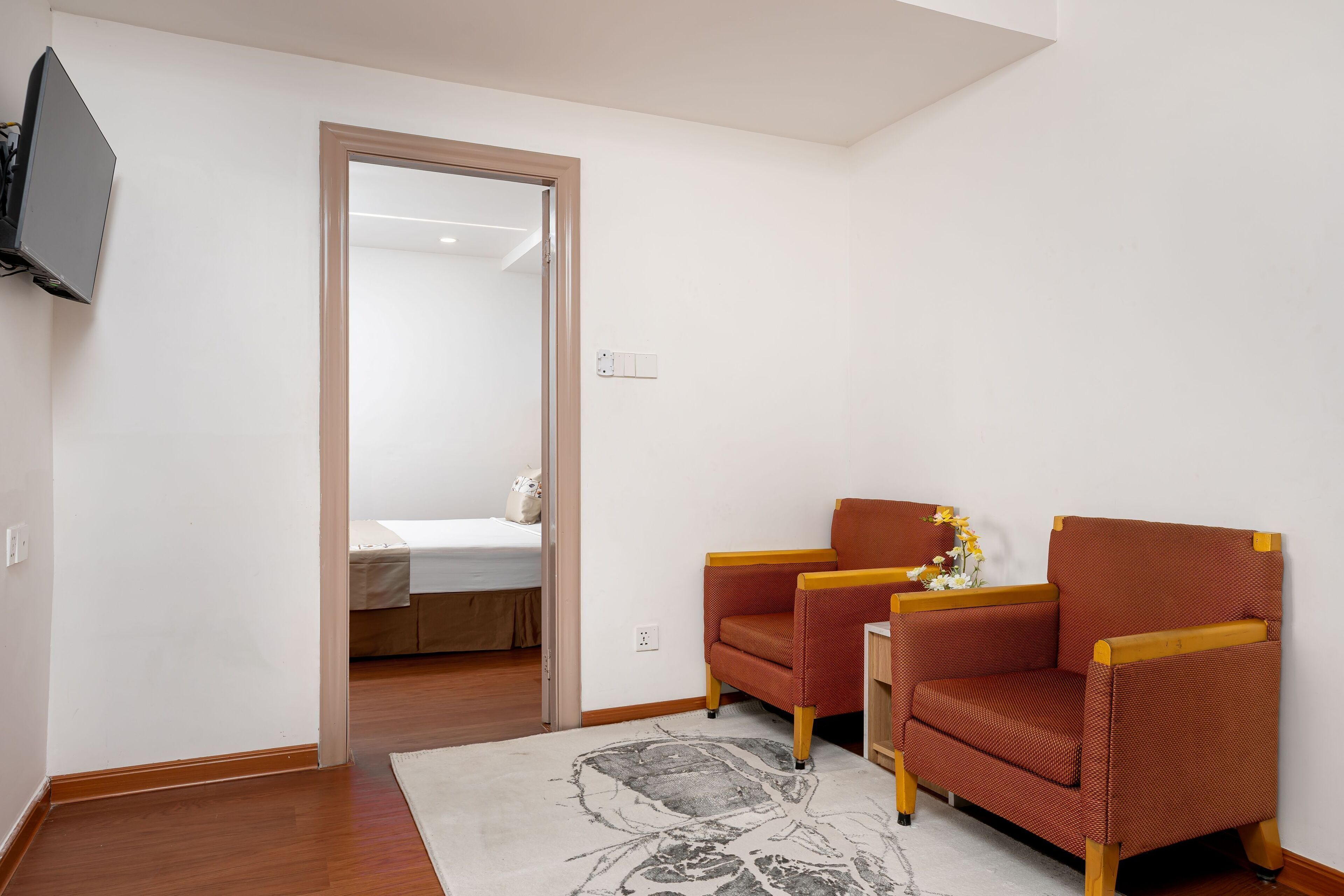 A room with two armchairs, a bed, and a television mounted on the wall.