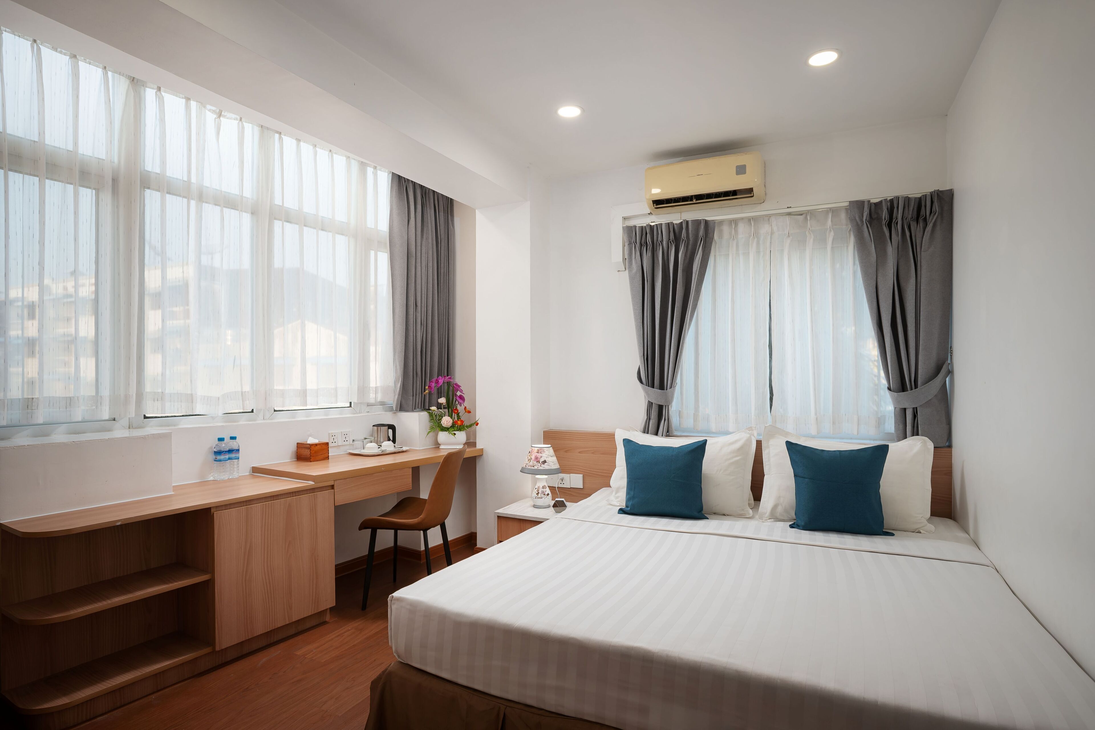 Et hotelværelse med seng, skrivebord, stol, lille bord og en aircondition.