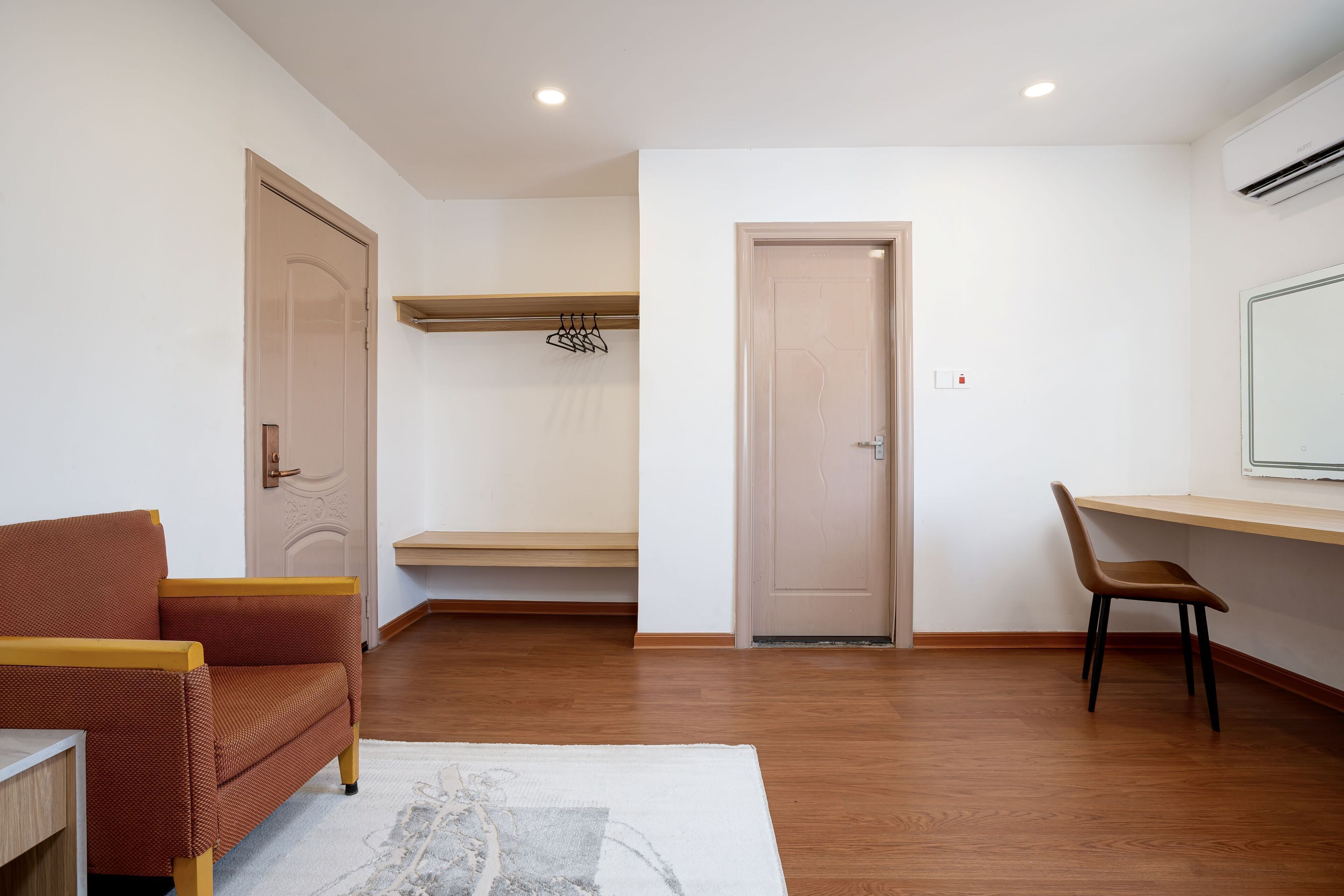 Una habitación con piso de madera, un sofá marrón, una silla, un escritorio y una puerta.
