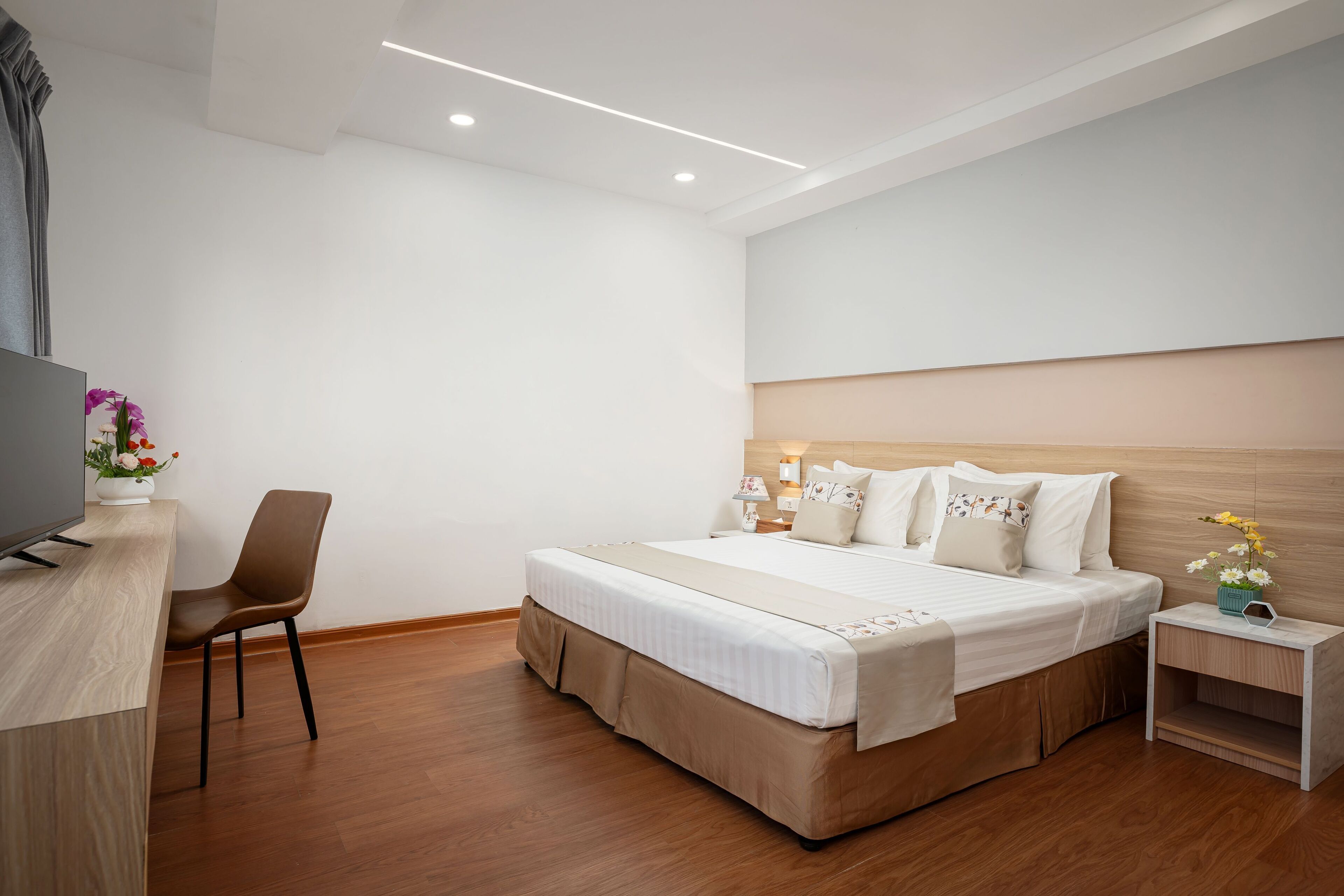 A modern hotel room with a large bed, a desk, a chair, and a TV.