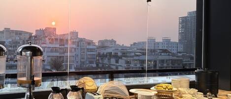 Un bar où l’on peut prendre le petit-déjeuner, avec des machines à café, un grille-pain et une vue sur le paysage urbain au coucher du soleil.