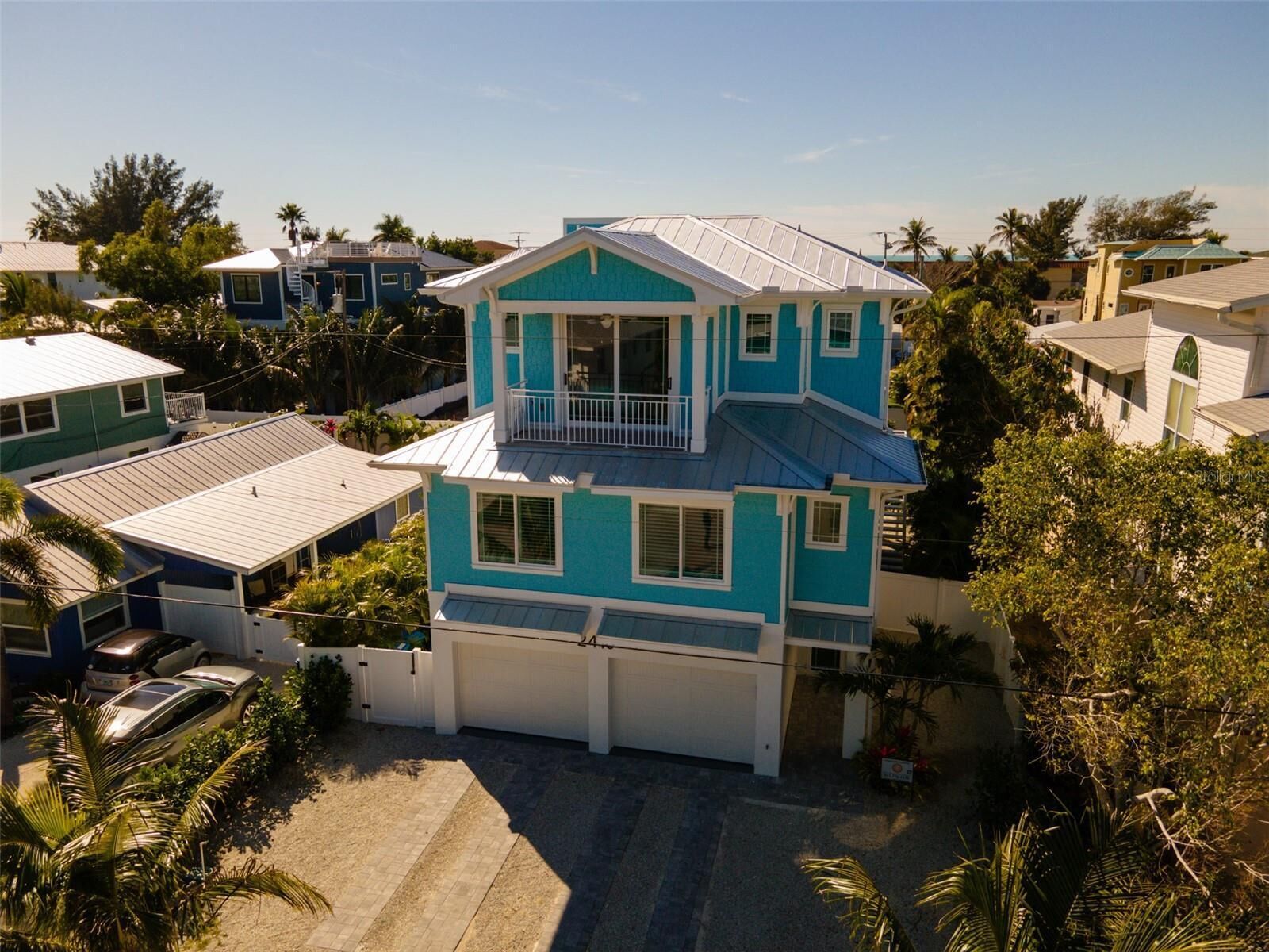 A two-story house with a balcony, surrounded by other houses and palm trees.