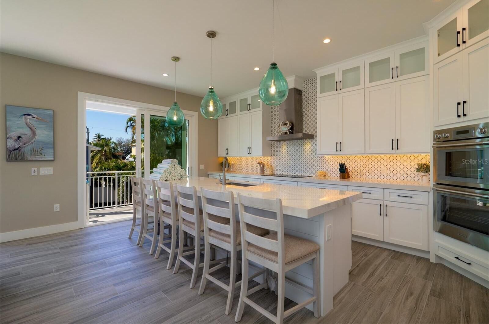 A modern kitchen with white cabinetry, a central island with bar stools, pendant lighting, and a view to the outdoors.