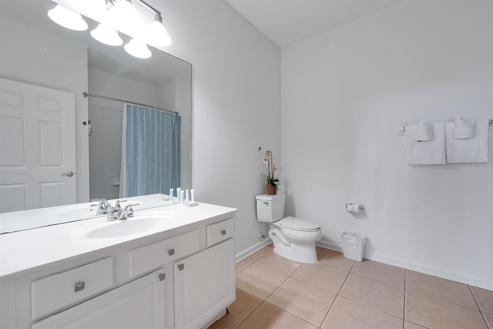 Een badkamer met een wit wastafel, spiegel en toilet. Er liggen toiletartikelen op het aanrecht en een prullenbak naast het toilet.