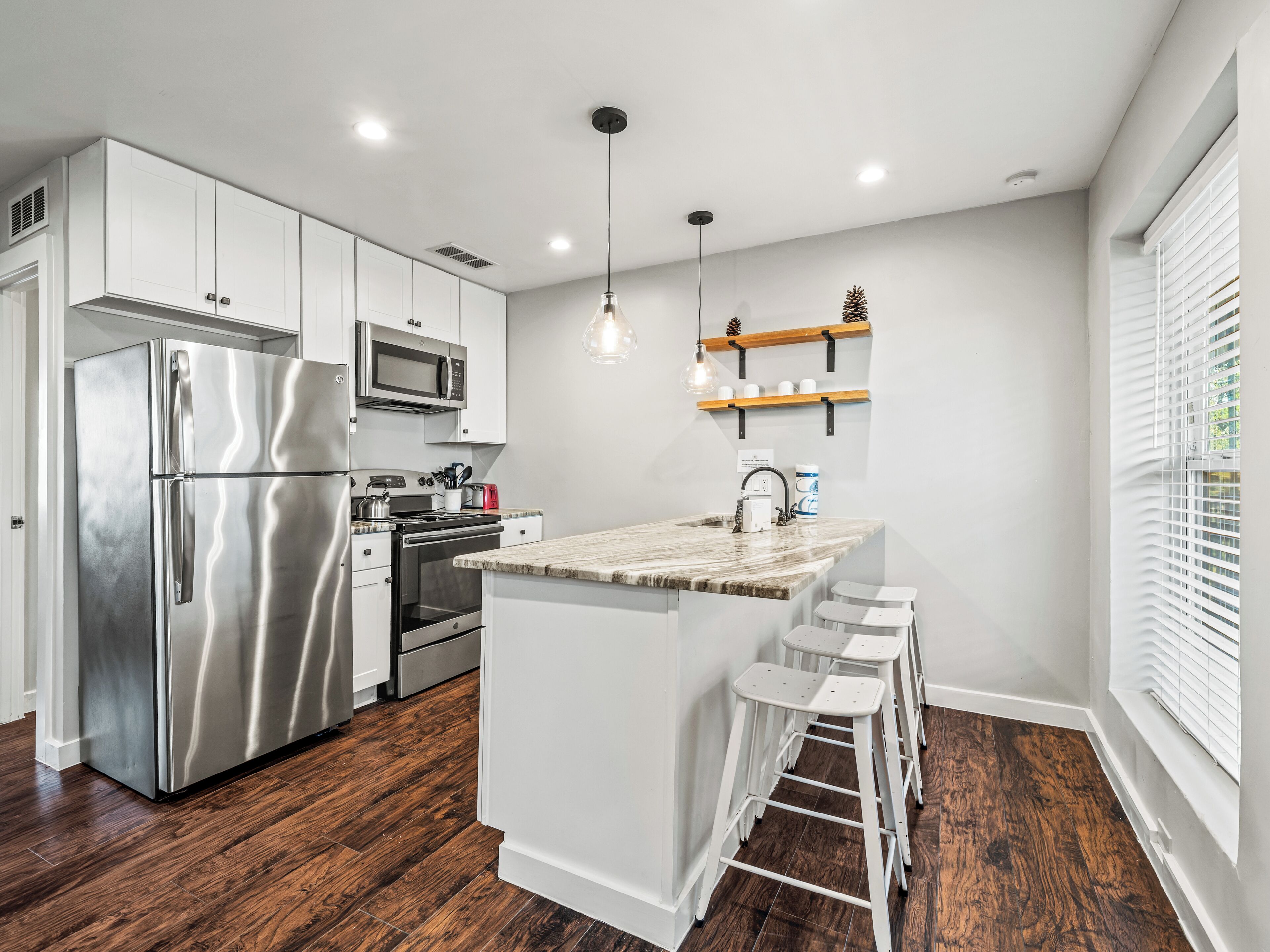 A modern kitchen with stainless steel appliances, a central island with bar stools, and a window with blinds.
