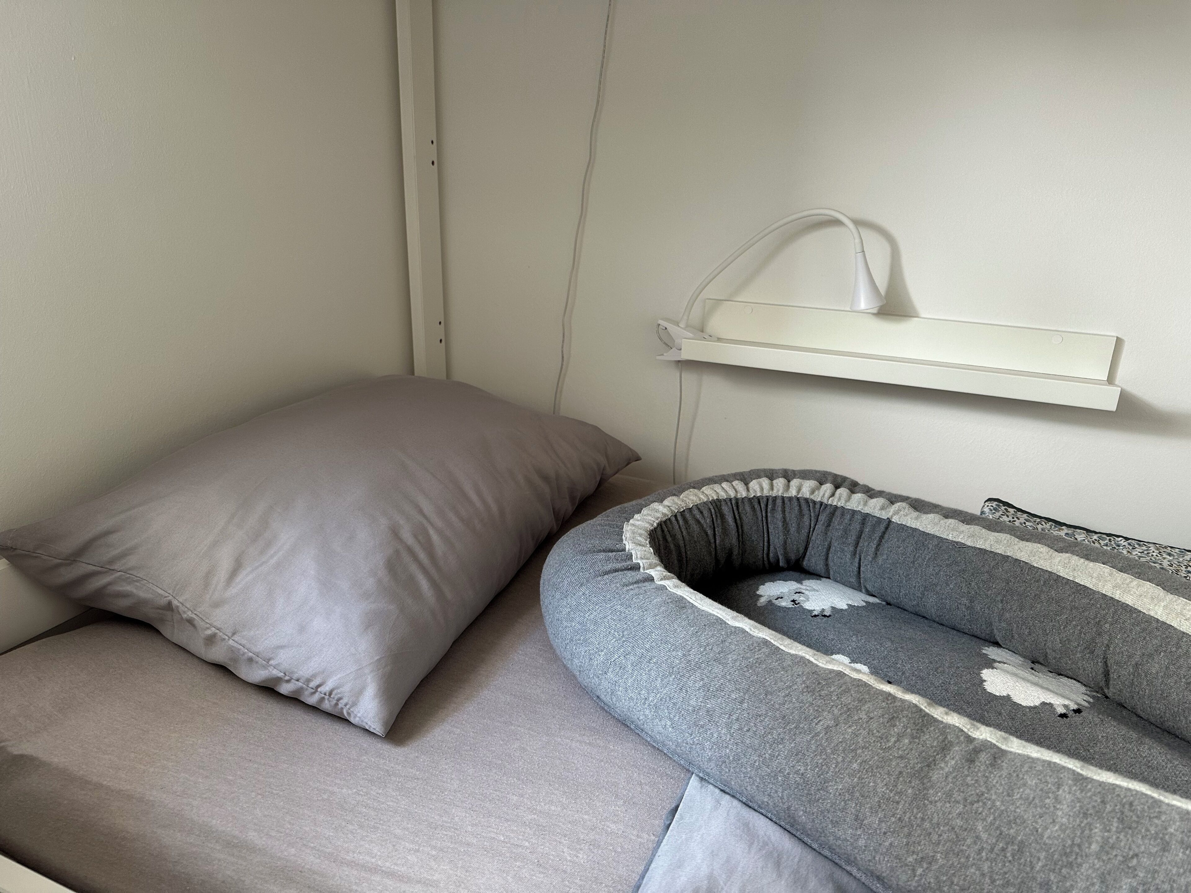 Una habitació amb un llit, un almoiner, una taula de nit i una prestatgeria penjada a la paret.