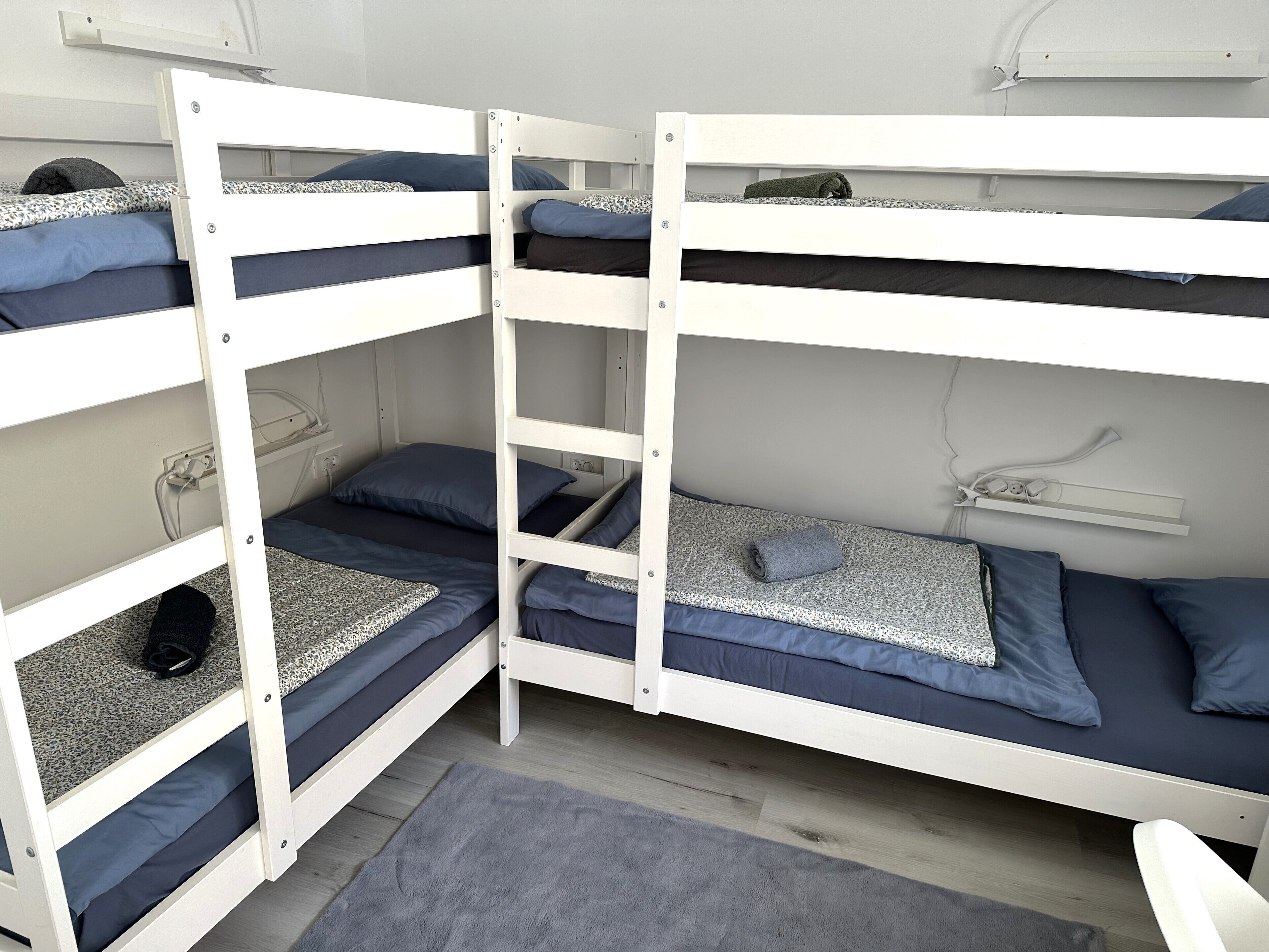 Quarto com beliche, tapete cinza, prateleira branca e tomada.