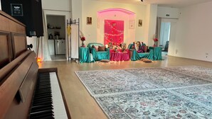 Un vaste espace de vie comprenant un piano, une grande moquette à motifs et un coin salon central avec des tables et des chaises.