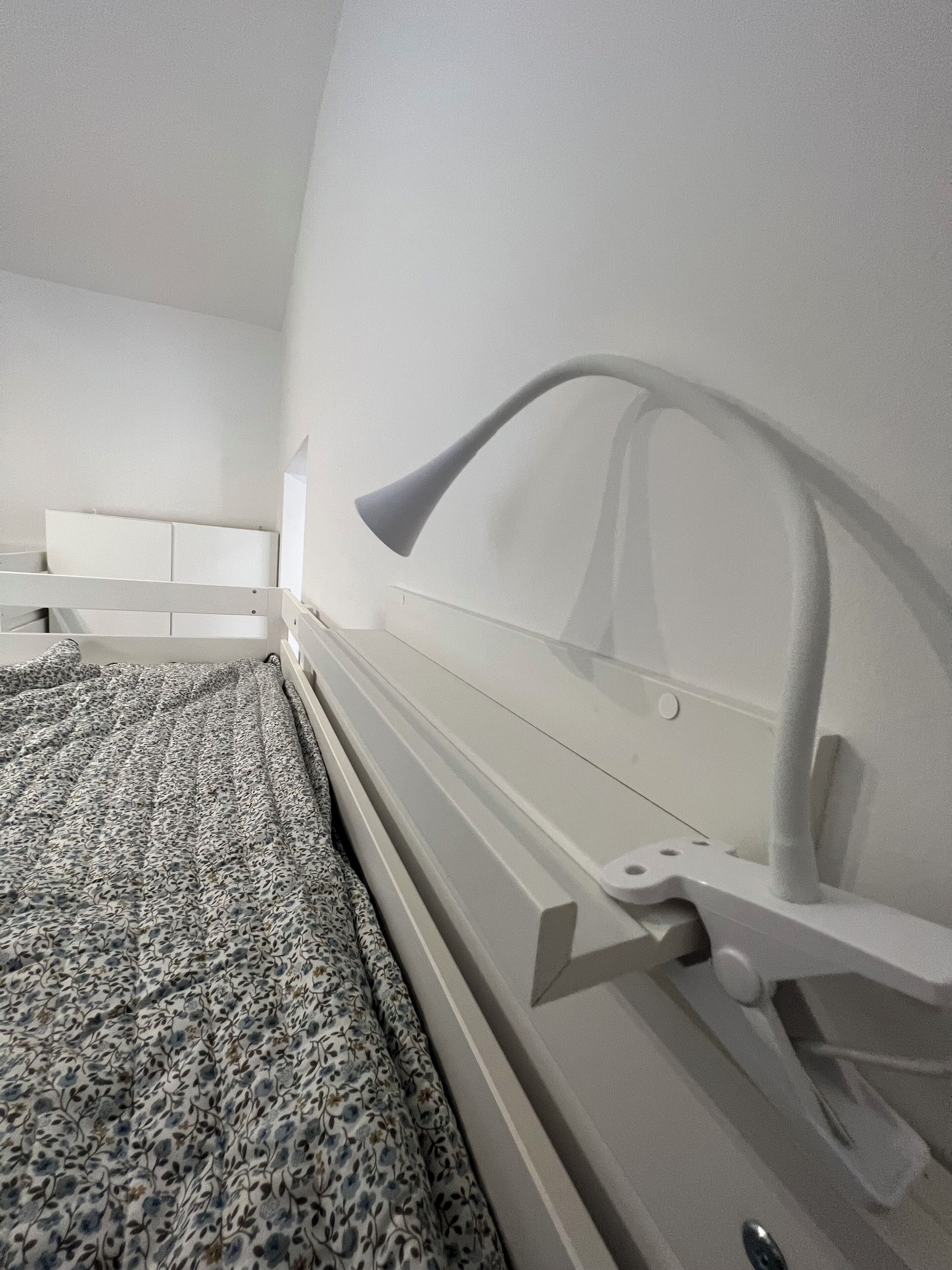 A bedroom with a bed, a headboard with a light fixture, and a patterned bedspread.