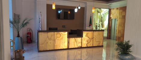 A reception area with a marble floor, a reception desk, and a wall-mounted TV.