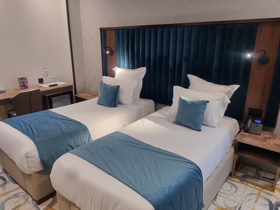 A hotel room with two beds, a desk, a telephone, and a patterned carpet.