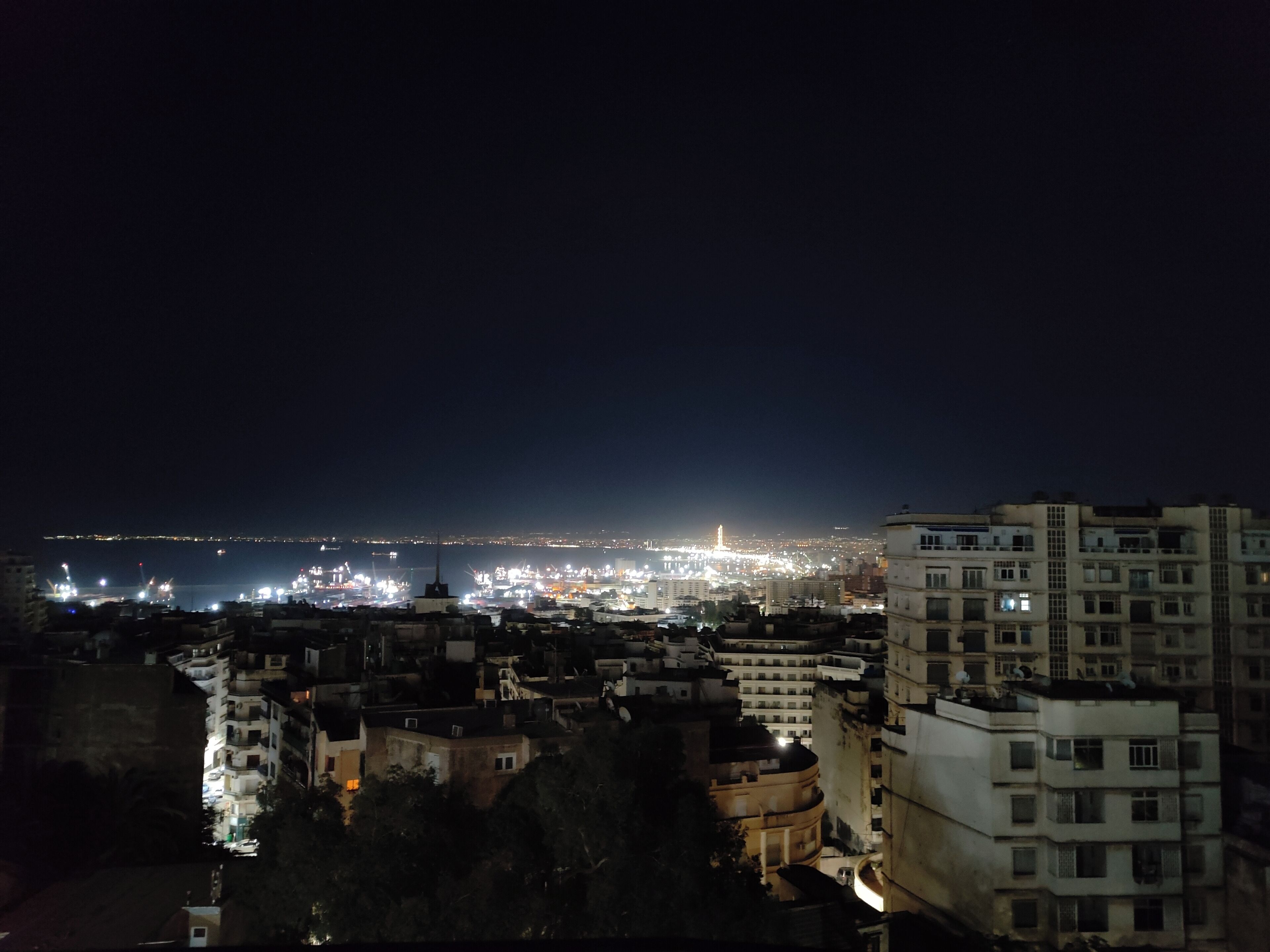 Un paisaje urbano nocturno con edificios iluminados y una vista distante del horizonte de la ciudad.