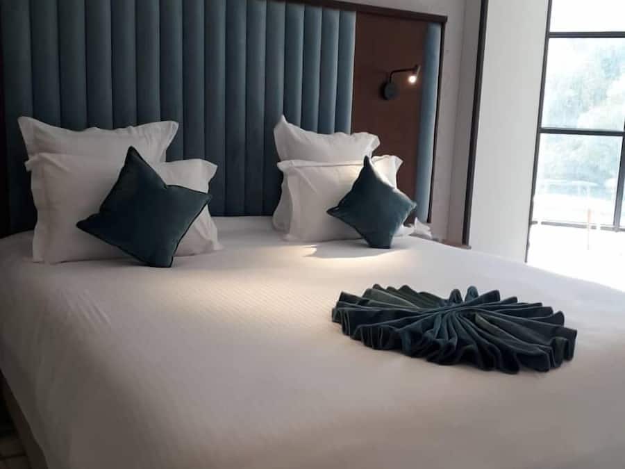 A modern hotel room with a large bed, a headboard with vertical slats, and a window providing a view of the outdoors.