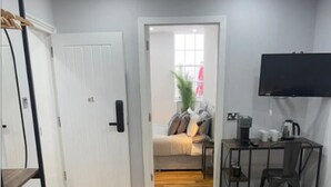 Ein kleines Hotelzimmer mit Bett, Schreibtisch mit Stuhl, Fernseher und einer kleinen Sitzecke mit Sofa und Kissen.