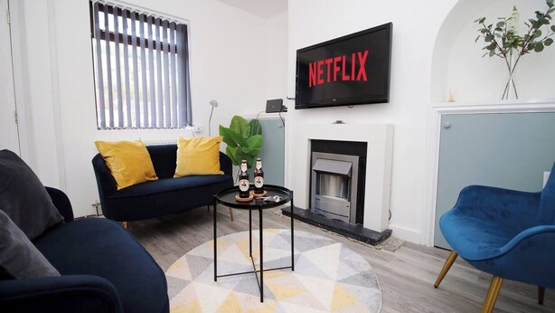 Una sala de estar con un sofá, una mesa de centro con botellas, una chimenea y un televisor mostrando "NETFLIX".