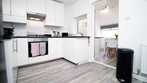 Una cocina moderna con armarios blancos, encimera negra y campana extractora de acero inoxidable. Se observa un cubo de basura negro y un radiador blanco en la esquina.