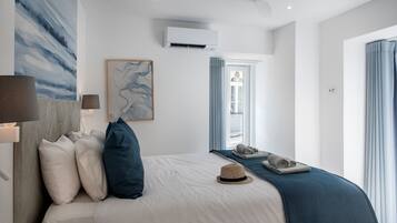 A modern hotel room with a bed, a wall-mounted air conditioner, a window with curtains, and a painting.
