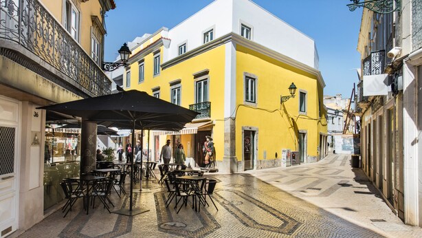 Rua com mesas ao ar livre, um edifício amarelo e um edifício branco.