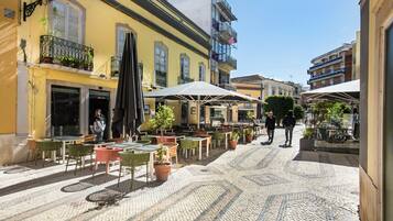 A cobblestone street with outdoor seating, potted plants, and a clear blue sky.
