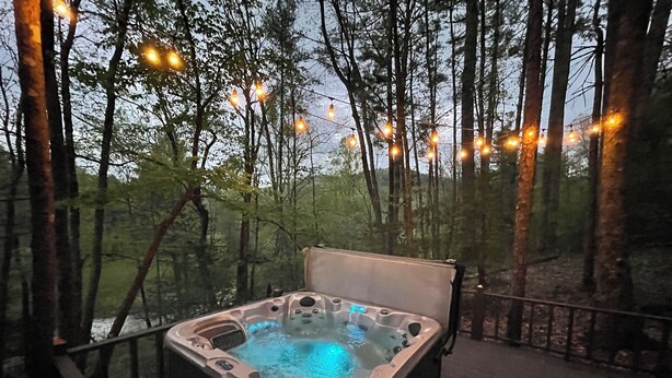 Un bain à remous sur une terrasse extérieure, entouré d’arbres, avec des guirlandes lumineuses suspendues au-dessus.