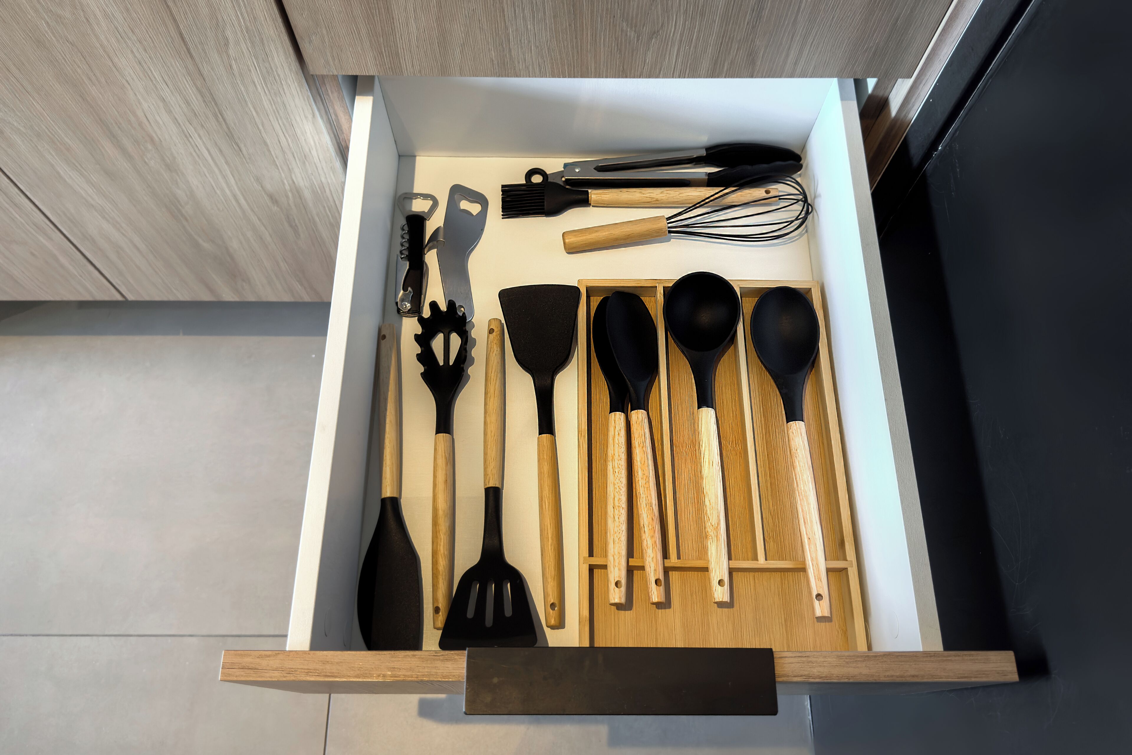 A drawer with various kitchen utensils including spatulas, whisks, and a grater.