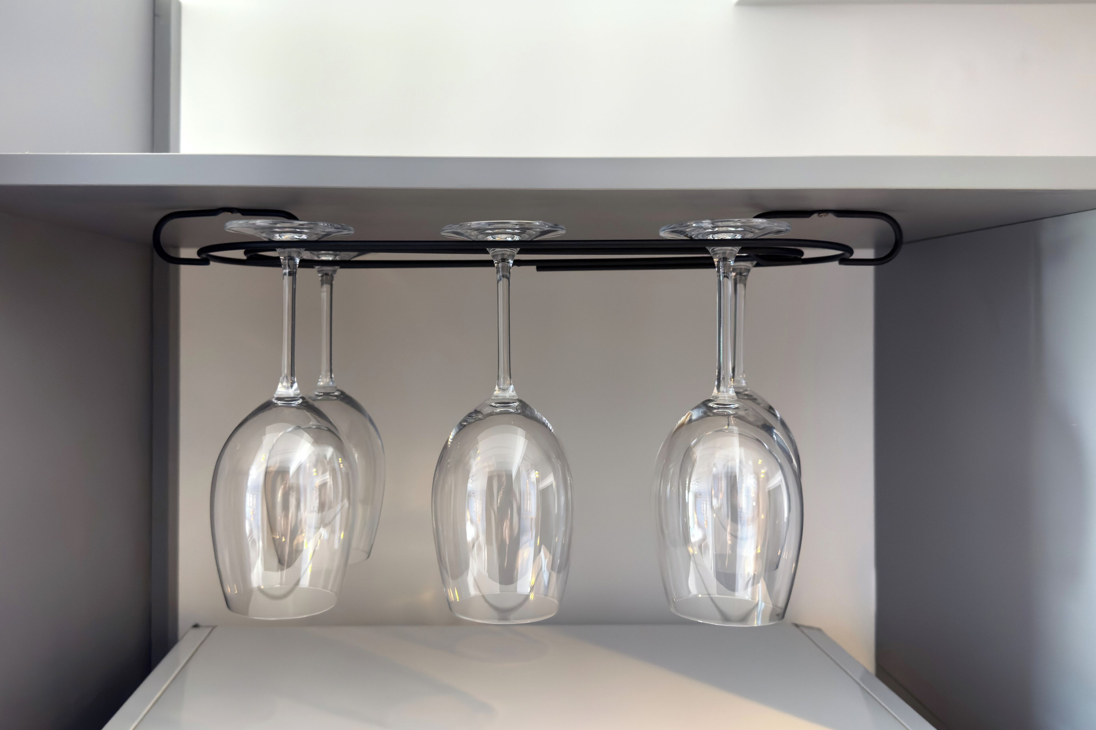 Three wine glasses hanging from a black bar on a white shelf.