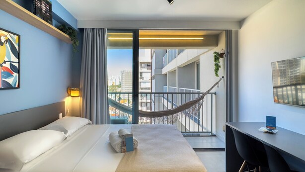 Una moderna camera d'albergo con un letto, una scrivania e un balcone con un'amaca.