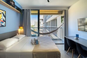 Une chambre d’hôtel moderne équipée d’un lit, d’un bureau et d’un balcon avec un hamac.