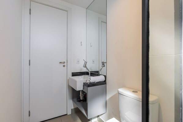 Une salle de bain avec des toilettes blanches, un lavabo avec un miroir et une porte.