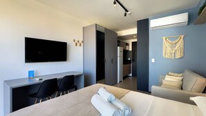 Una camera d'albergo moderna con un letto, una scrivania, una TV a schermo piatto e un angolo cottura.