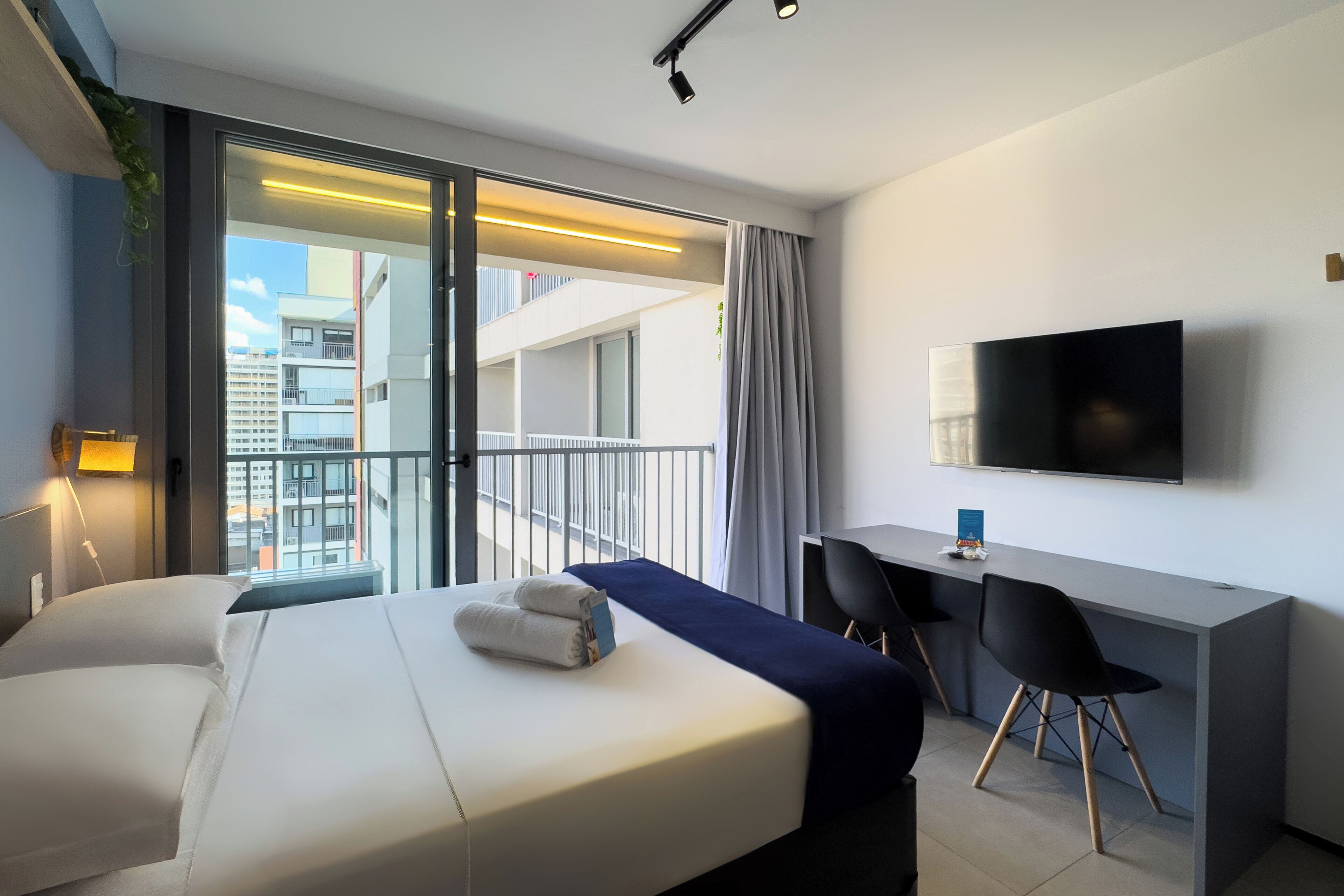 Moderni hotellihuone, jossa on sänky, työpöytä ja televisio.