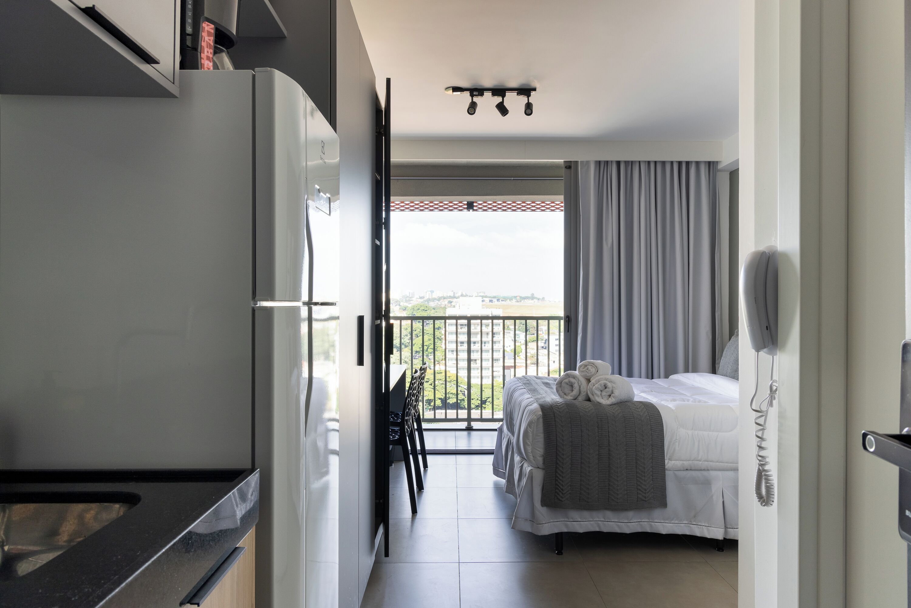 A hotel room with a balcony, a bed with towels, a desk, and a phone.