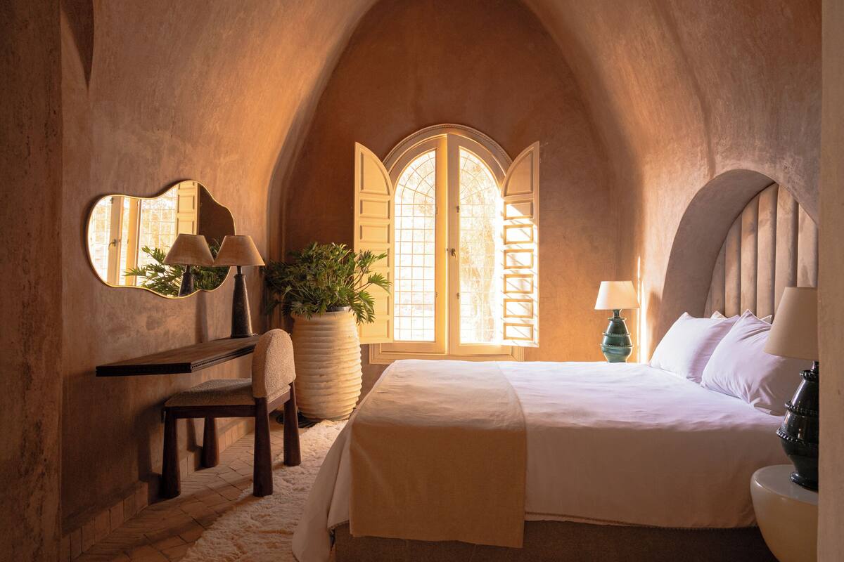 Un dormitorio con cama, escritorio, silla, planta en maceta y un gran ventanal de arco.