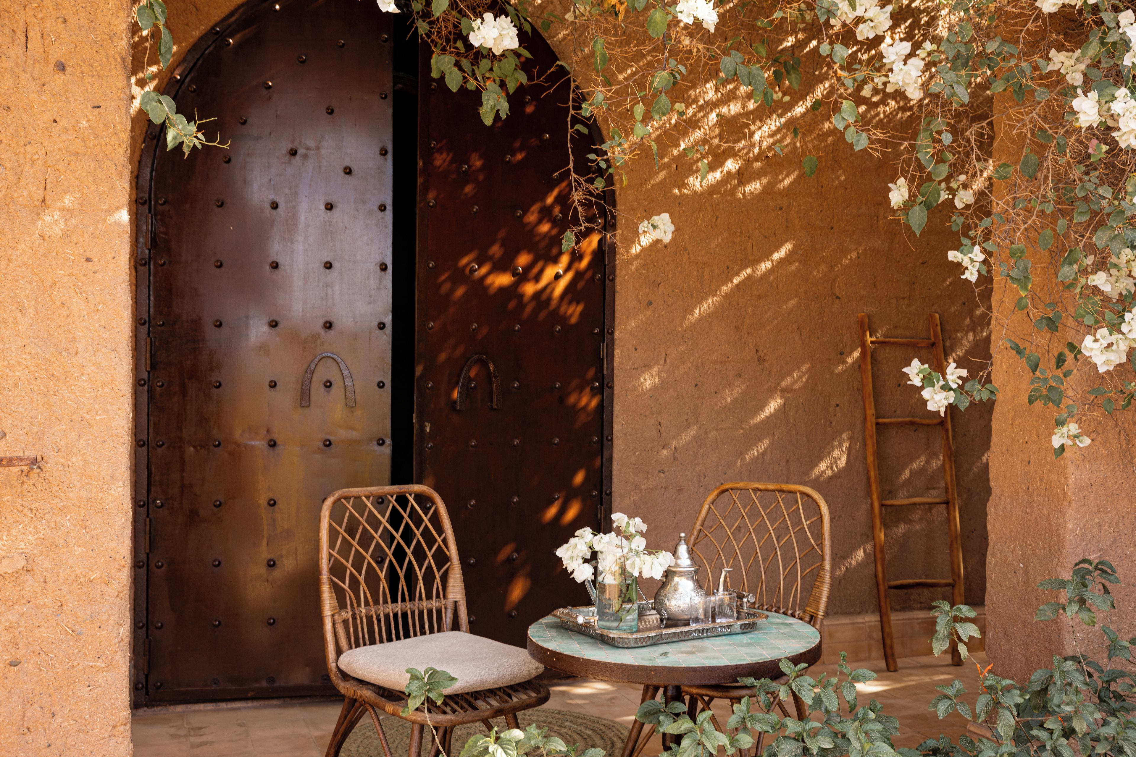 A rustic outdoor seating area with two wicker chairs, a small round table, and a metal tray.