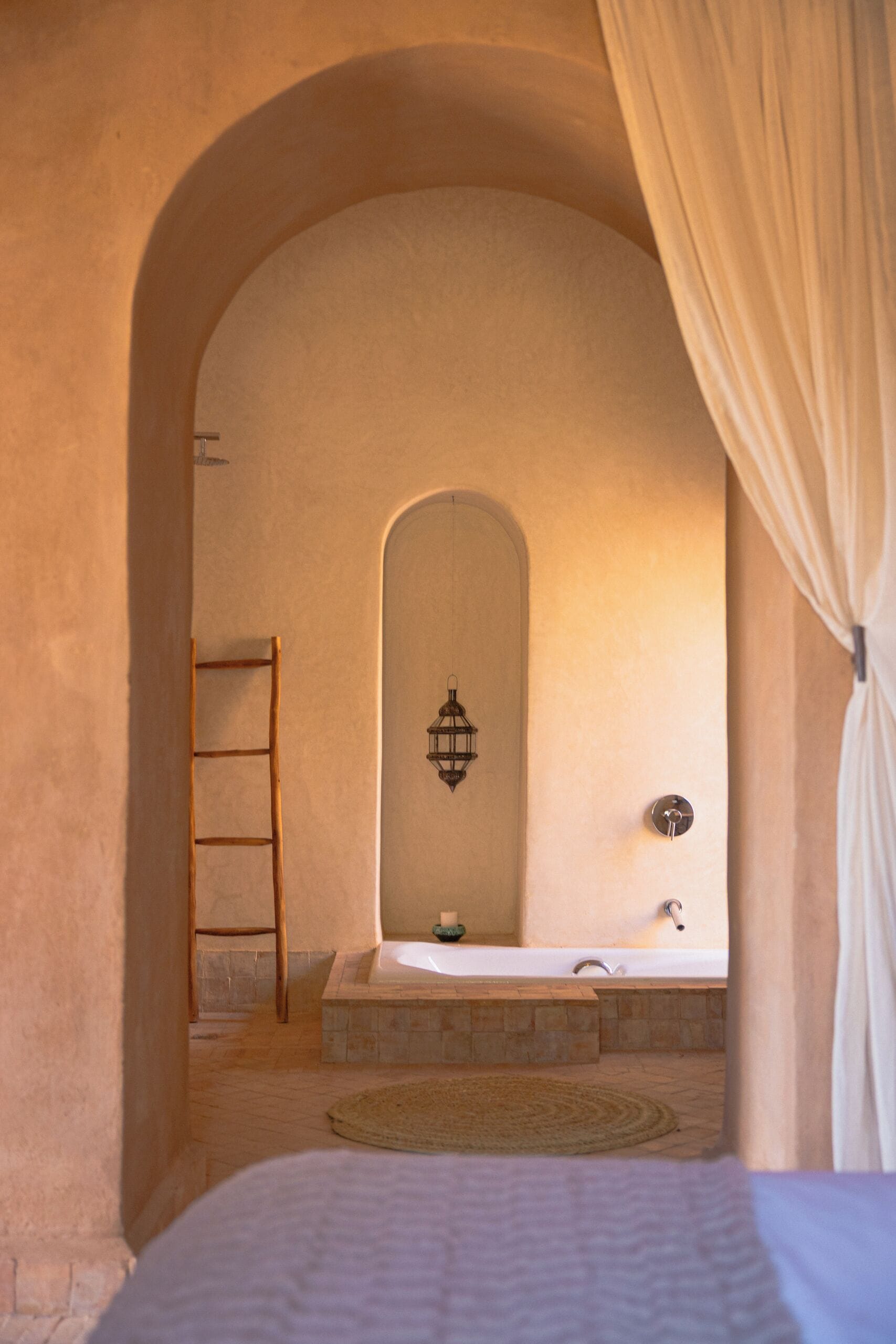 A bedroom with a bed, a wooden ladder, a bathtub, and a wall-mounted light fixture.