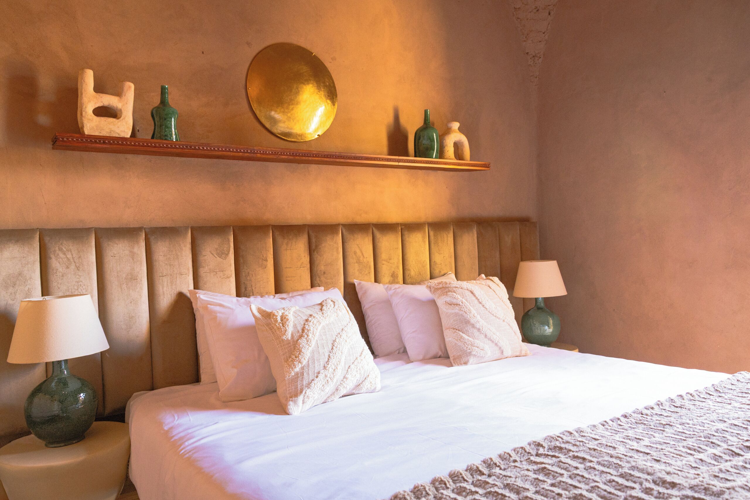 Une chambre d’hôtel avec un grand lit, deux lampes de chevet, une tête de lit en bois et une étagère ornée d’objets décoratifs.