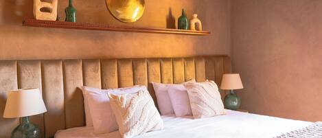Habitación de hotel con una cama grande, dos lámparas de noche, un cabecero de madera y una estantería con objetos decorativos.