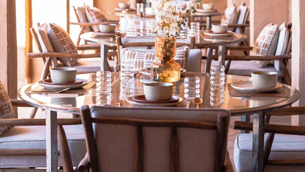 A dining area with a long table set for a meal, surrounded by arches and a view through a window. - Bliss Terra Janna (Marrakech)