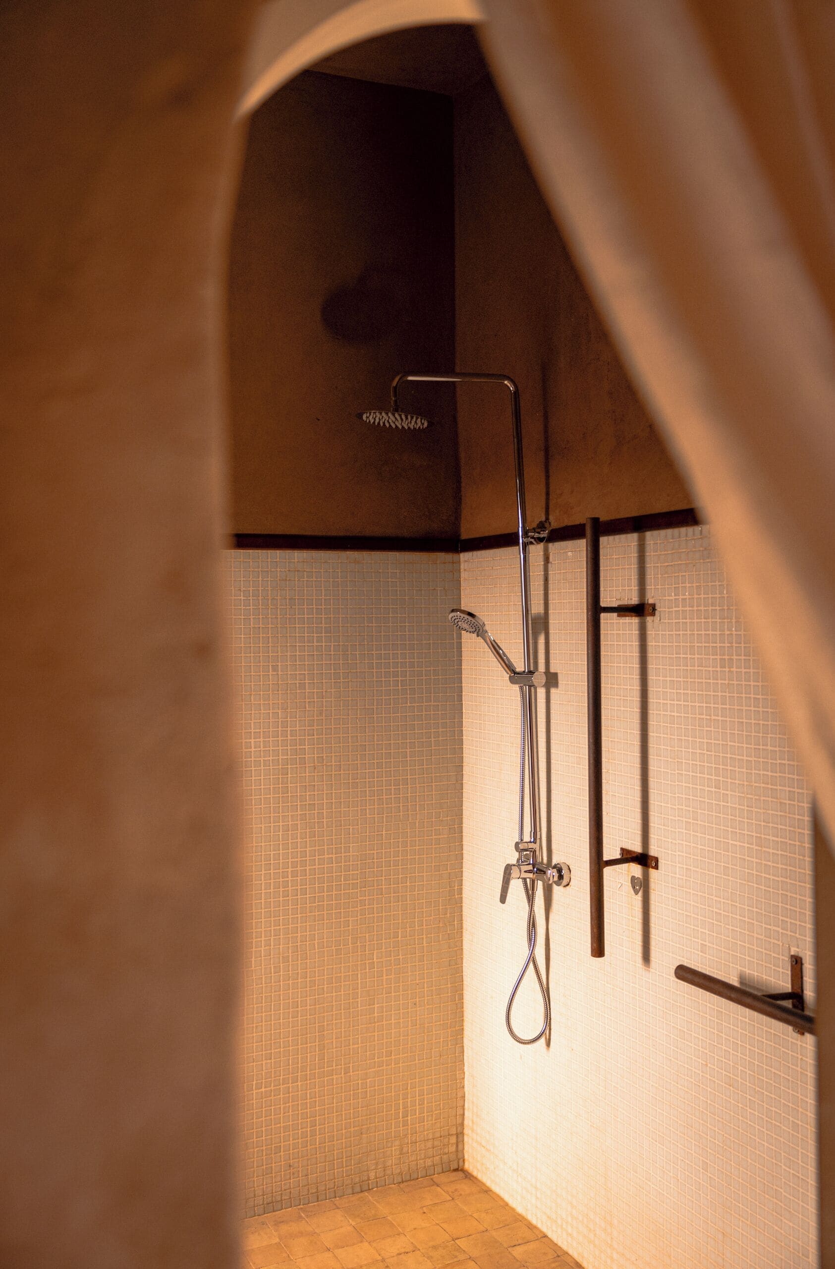 A small, tiled shower area with a showerhead and controls mounted on the wall.