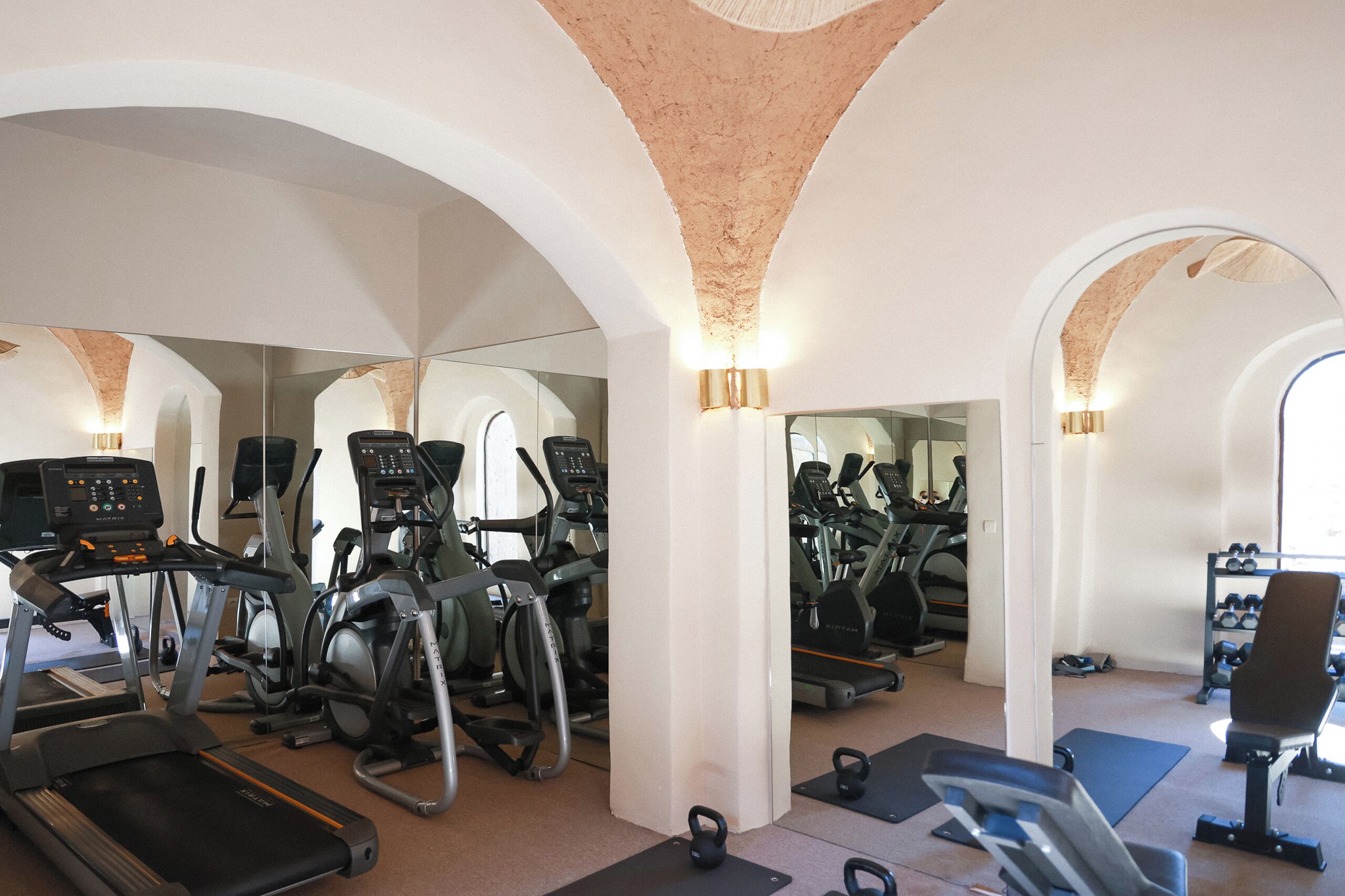 A gym with treadmills, elliptical machines, and free weights, featuring arched ceilings and mirrored walls.