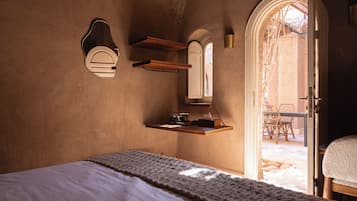 A bedroom with a bed, a wooden shelf with a mirror, and a door leading to an outdoor area with a table and chairs.