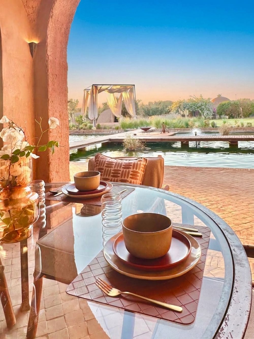A table set for dining with a view of a landscaped garden and a body of water.