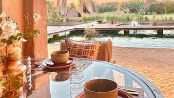A table set for dining with a view of a landscaped garden and a body of water.